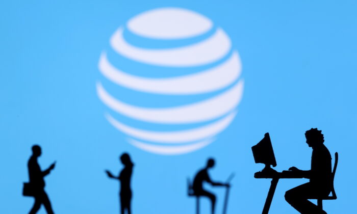 Small toy figures with laptops and smartphones are seen in front of  a displayed AT&T logo, in this illustration taken on Dec. 5, 2021. (Dado Ruvic/Illustration/Reuters)