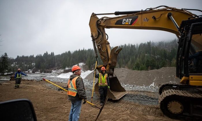 Construction workers stand in the northbound lanes of the Coquihalla Highway where a massive section of the separate southbound lanes was washed away by flooding last month near Othello northeast of Hope, B.C., Dec. 10, 2021. (The Canadian Press/Darryl Dyck)