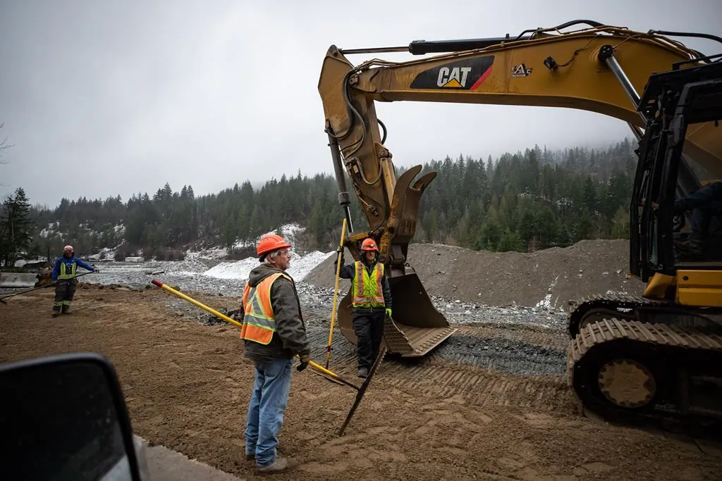 Construction workers stand in the northbound lanes of the Coquihalla Highway where a massive section of the separate southbound lanes was washed away by flooding last month near Othello northeast of Hope, B.C., Dec. 10, 2021. (The Canadian Press/Darryl Dyck)