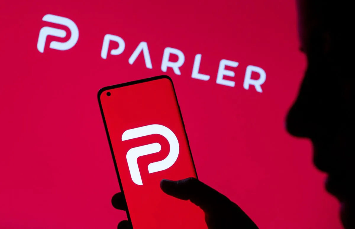 A photo illustration showing a woman holding her smartphone with Parler logo, in front of displayed same logo, on May 17, 2021. (Dado Ruvic/Reuters)