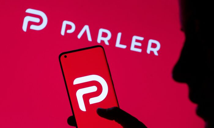 A photo illustration showing a woman holding her smartphone with Parler logo, in front of displayed same logo, on May 17, 2021. (Dado Ruvic/Reuters)