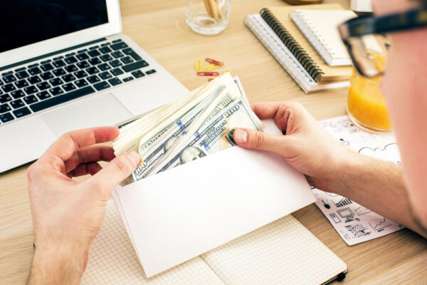 Man,Holding,Envelope,With,Money,Above,Wooden,Office,Desktop,With