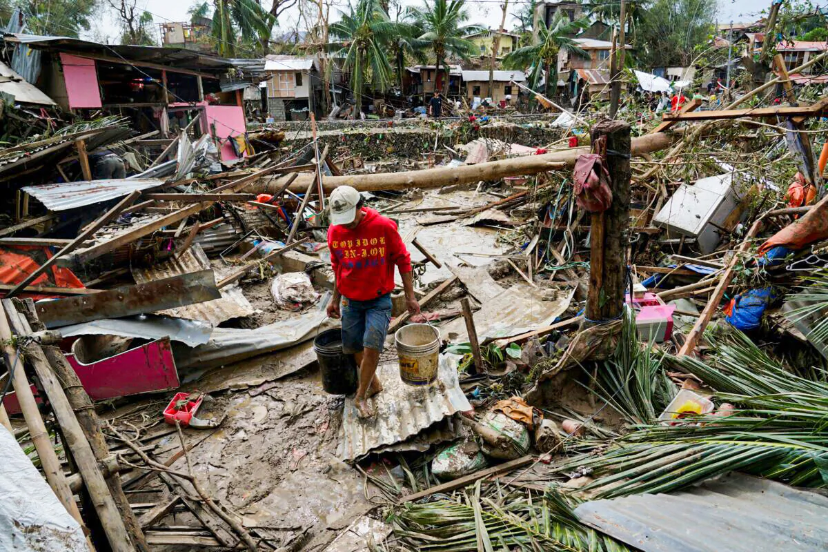 A man carries pails beside damaged homes due to Typhoon Rai in Talisay, Cebu province, central Philippines, on Dec. 17, 2021. (Jay Labra/AP Photo)