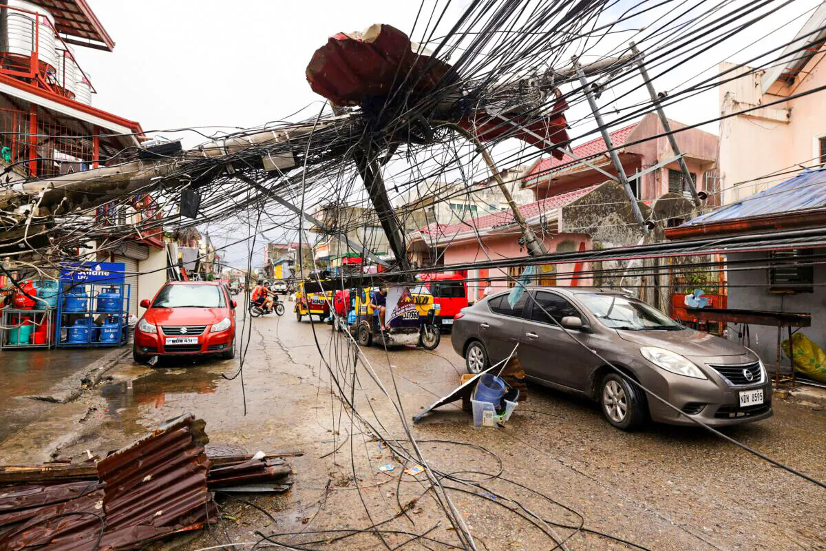 Cars pass by a toppled electrical post due to Typhoon Rai in Surigao city, Surigao del Norte, the southern Philippines as power supply remains down on Dec. 19, 2021. (Jilson Tiu/AP Photo)