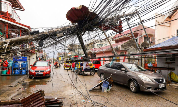 Cars pass by a toppled electrical post due to Typhoon Rai in Surigao city, Surigao del Norte, the southern Philippines as power supply remains down on Dec. 19, 2021. (Jilson Tiu/AP Photo)