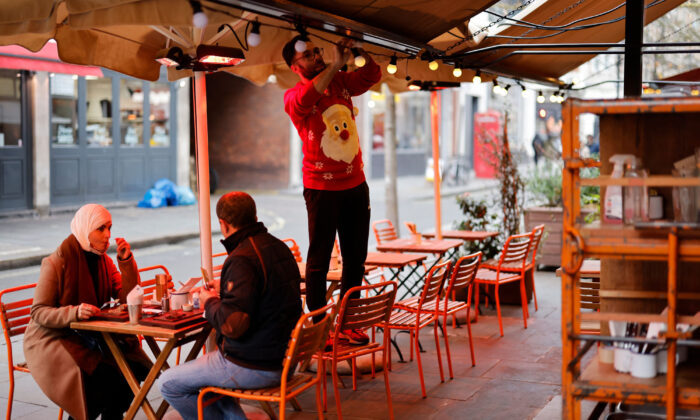 A hospitality worker wearing a Santa-themed Christmas jumper works around empty tables outside a restaurant in London on Dec. 21, 2021. (Tolga Akmen/AFP via Getty Images)