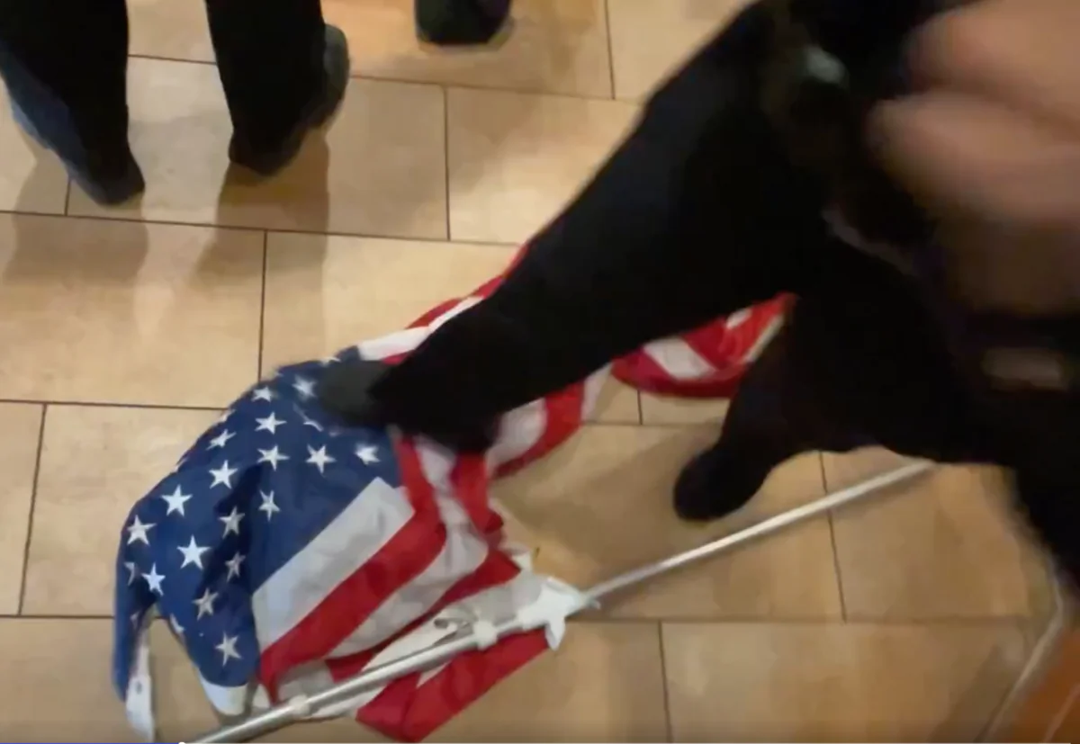 An NYPD officer steps on the U.S. flag at a Panera Bread in Brooklyn, New York, on Dec. 19, 2021. (Courtesy of Chris Wright)