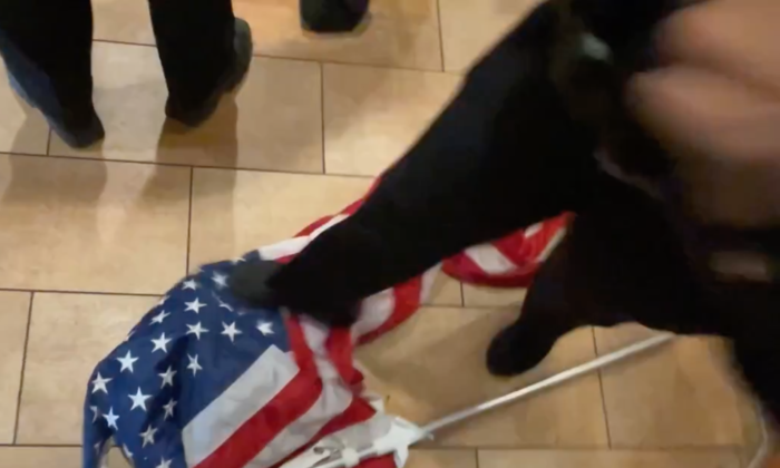 An NYPD officer steps on the U.S. flag at a Panera Bread in Brooklyn, New York, on Dec. 19, 2021. (Courtesy of Chris Wright)
