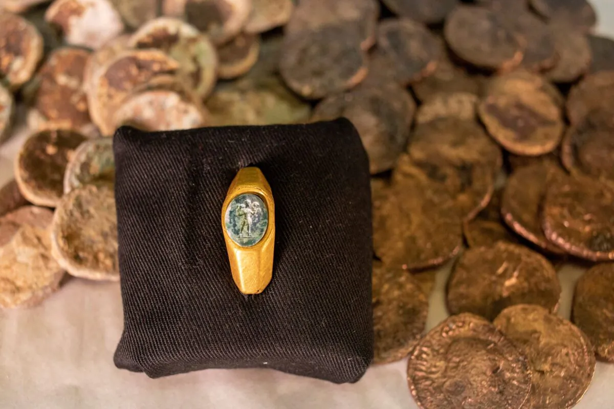Roman gold ring, its green gemstone carved with the figure of a shepherd carrying a sheep on his shoulders is on display with coins that were found near the ancient city of Caesarea, dated to the Roman and Mamluk periods, around 1,700 and 600 years ago, in Jerusalem, on Dec. 22, 2021. (Ariel Schalit/AP Photo)