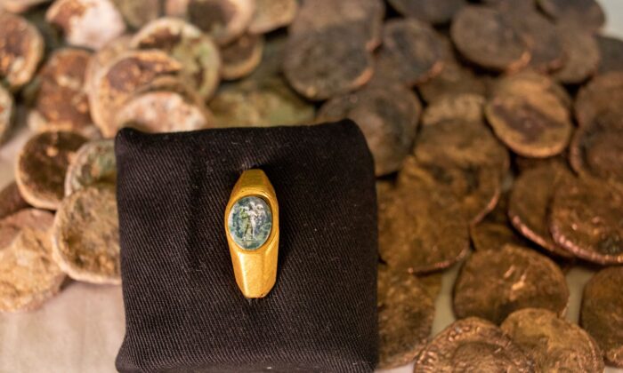 Roman gold ring, its green gemstone carved with the figure of a shepherd carrying a sheep on his shoulders is on display with coins that were found near the ancient city of Caesarea, dated to the Roman and Mamluk periods, around 1,700 and 600 years ago, in Jerusalem, on Dec. 22, 2021. (Ariel Schalit/AP Photo)