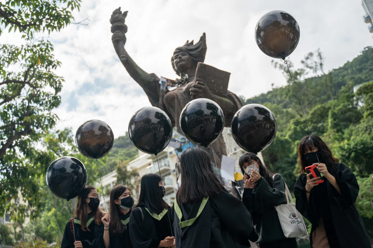 Students wearing black graduation gowns and masks stand in front of the Goddess of Democracy statue at the Chinese University of Hong Kong campus as they hold up black balloons in Hong Kong, China, on Nov. 19, 2020. (Anthony Kwan/Getty Images)