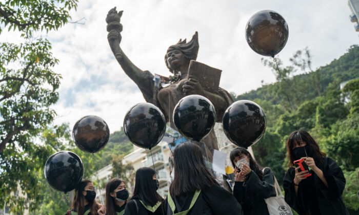 Students wearing black graduation gowns and masks stand in front of the Goddess of Democracy statue at the Chinese University of Hong Kong campus as they hold up black balloons in Hong Kong, China, on Nov. 19, 2020. (Anthony Kwan/Getty Images)