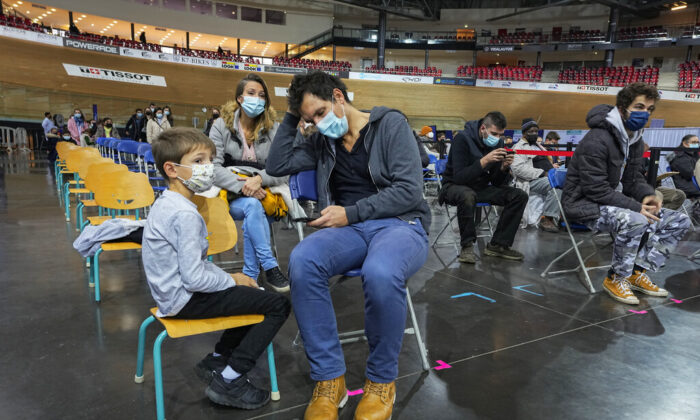 Hugo Chappaz, 9, left, waits with his father Benoit Chappaz, right, and his mother to be vaccinated at the National Velodrome in Saint-Quentin-en-Yvelines, west of Paris, France on Dec. 22, 2021. (Michel Euler/ AP Photo)