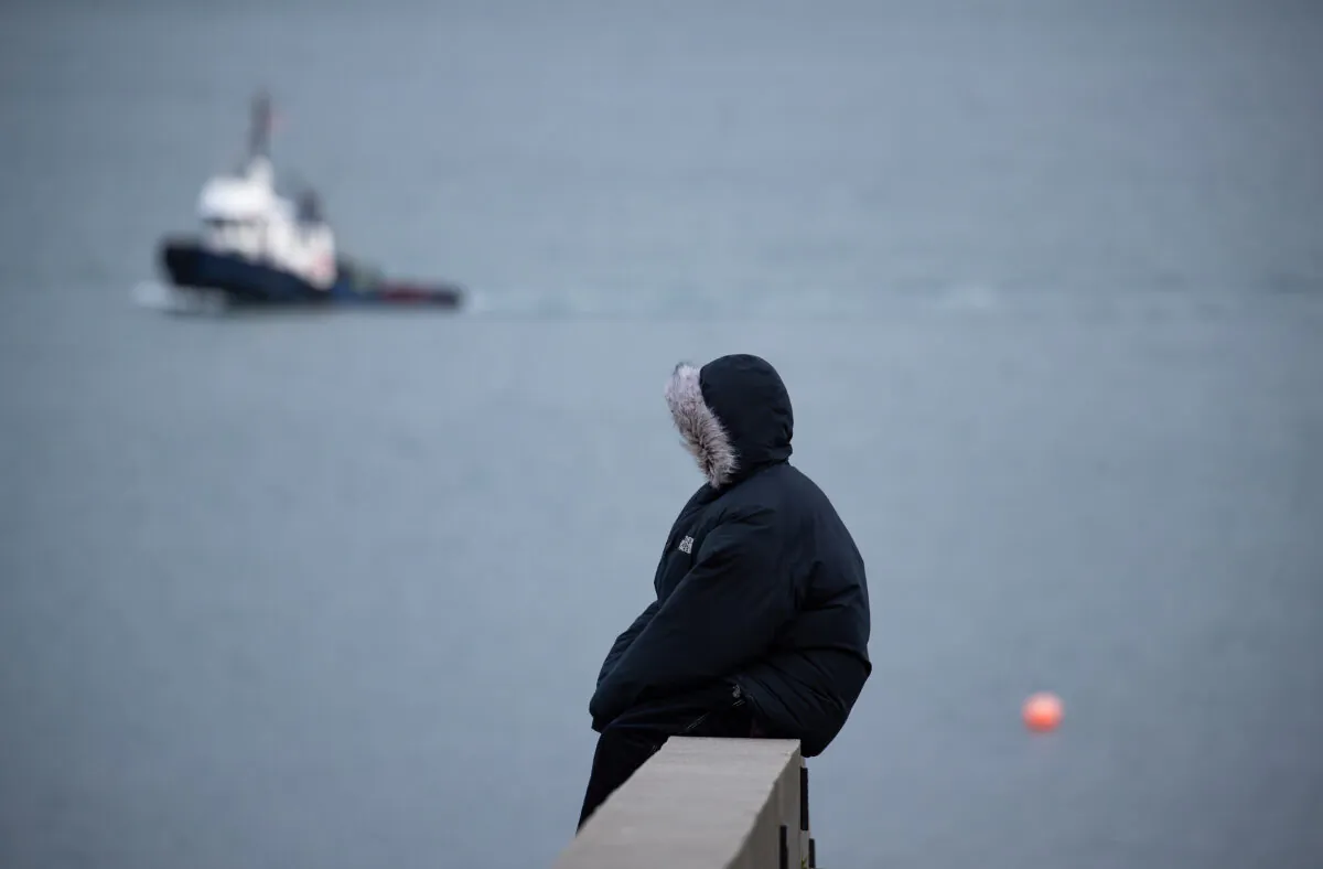 A person wearing a parka sits on the harbour in Vancouver, on Dec. 23, 2021. Environment Canada issued warnings of extreme cold and arctic outflow across British Columbia after Boxing Day. (Darryl Dyck/The Canadian Press)