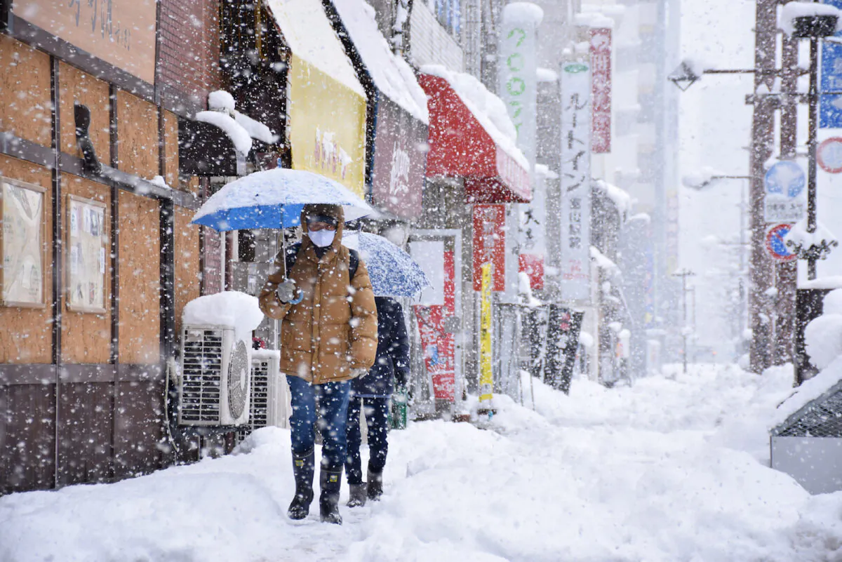 People walk along a street in heavy snow in Toyama, Japan, brought by an extreme cold front along western and northern parts of the country on Dec. 27, 2021. (JIJI Press/AFP via Getty Images)