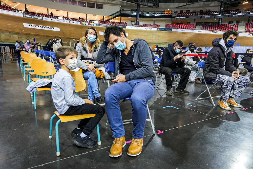 Hugo Chappaz, 9, left, waits with his father Benoit Chappaz, right, and his mother to be vaccinated at the National Velodrome in Saint-Quentin-en-Yvelines, west of Paris, France on Dec. 22, 2021. (Michel Euler/ AP Photo)