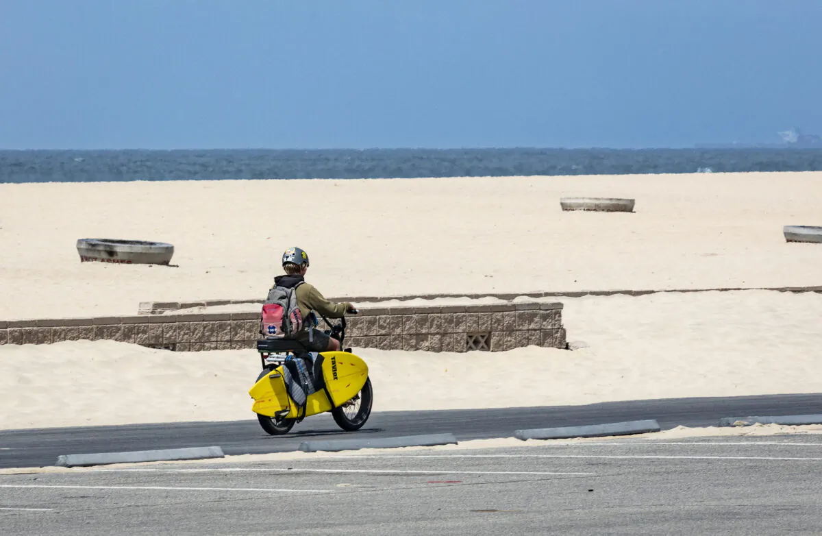 A boy rides an E-Bike with his surfboard along the beach in Huntington Beach, Calif., on May 20, 2021. (John Fredricks/The Epoch Times)
