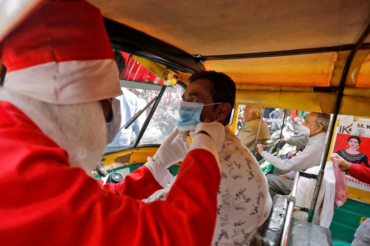 A man wearing a Santa Claus costume helps an auto rickshaw driver to wear a protective face mask as he distributes the masks for free during the ongoing coronavirus disease (COVID-19) pandemic, in Ahmedabad, India, on Dec. 24, 2021. (Amit Dave/Reuters)