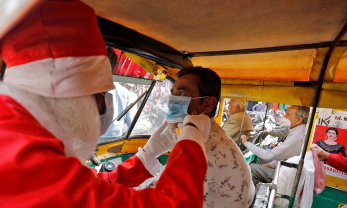 A man wearing a Santa Claus costume helps an auto rickshaw driver to wear a protective face mask as he distributes the masks for free during the ongoing coronavirus disease (COVID-19) pandemic, in Ahmedabad, India, on Dec. 24, 2021. (Amit Dave/Reuters)