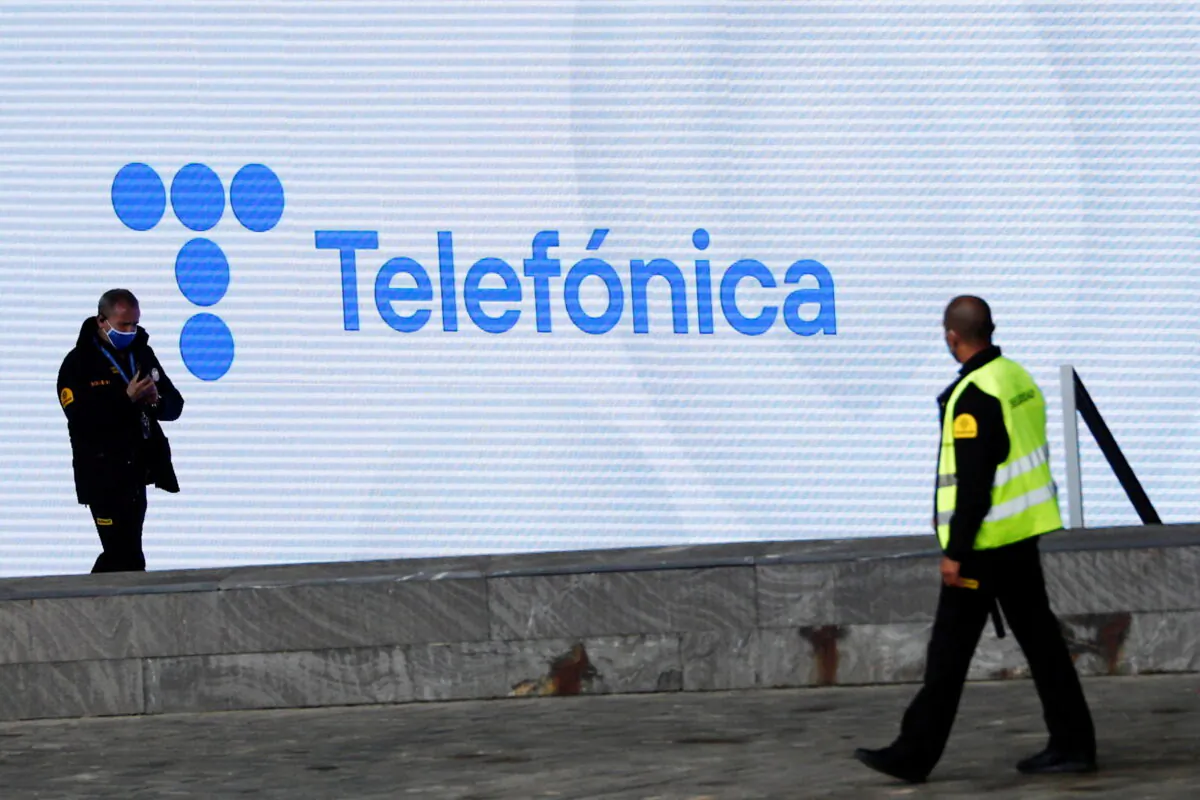 Security guards walk past a screen displaying the logo of Spanish Telecom company Telefónica at its headquarters in Madrid, Spain, on May 12, 2021. (Sergio Perez/Reuters)