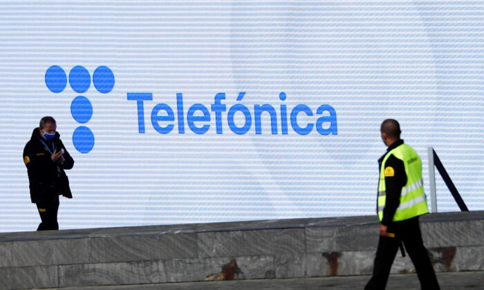 Security guards walk past a screen displaying the logo of Spanish Telecom company Telefonica at its headquarters in Madrid, Spain, on May 12, 2021. (Sergio Perez/Reuters)