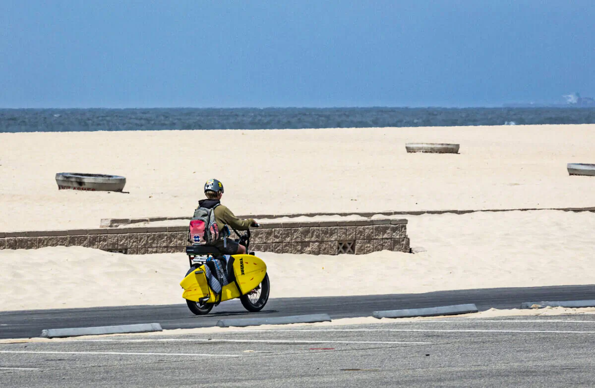 A boy rides an E-Bike with his surfboard along the beach in Huntington Beach, Calif., on May 20, 2021. (John Fredricks/The Epoch Times)