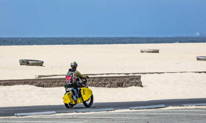 A boy rides an e-bike with his surfboard along the beach in Huntington Beach, Calif., on May 20, 2021. (John Fredricks/The Epoch Times)