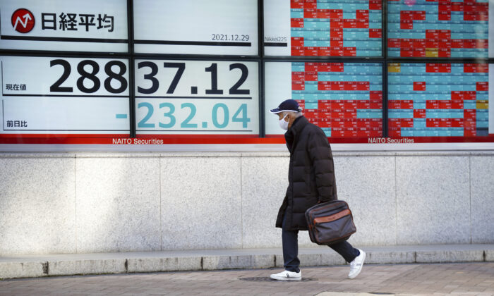A man wearing a protective mask rides a bicycle in front of an electronic stock board showing Japan's Nikkei 225 index at a securities firm in Tokyo on Dec. 29, 2021. (Eugene Hoshiko/AP Photo)
