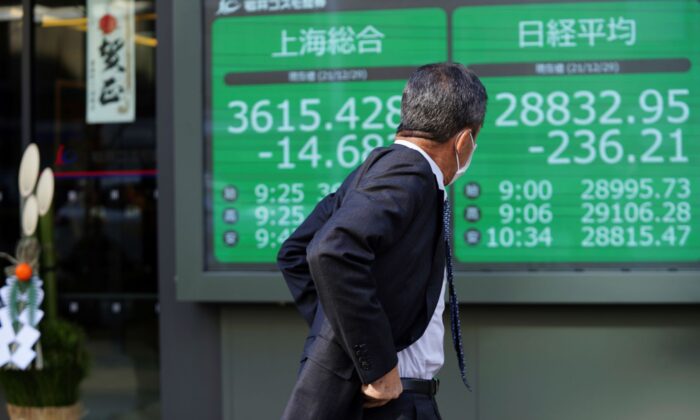 A man wearing a protective mask looks at an electronic stock board showing Japan's Nikkei 225 and Shanghai indexes at a securities firm with a traditional New Year decoration at its entrance in Tokyo, Japan, on Dec. 29, 2021. (Eugene Hoshiko/AP Photo)
