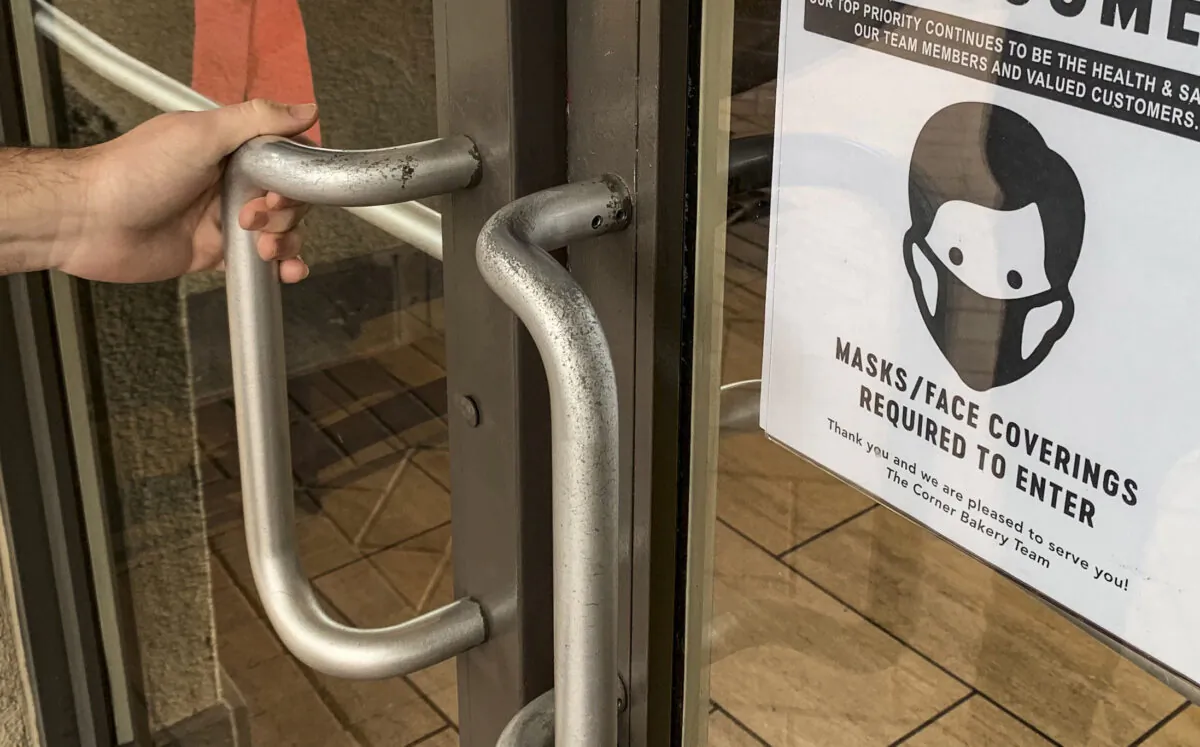 A sign for mask requirements is diplayed upon the entryway to a Corner Bakery restaurant in Irvine, Calif., on Dec. 29, 2021. (John Fredricks/The Epoch Times)