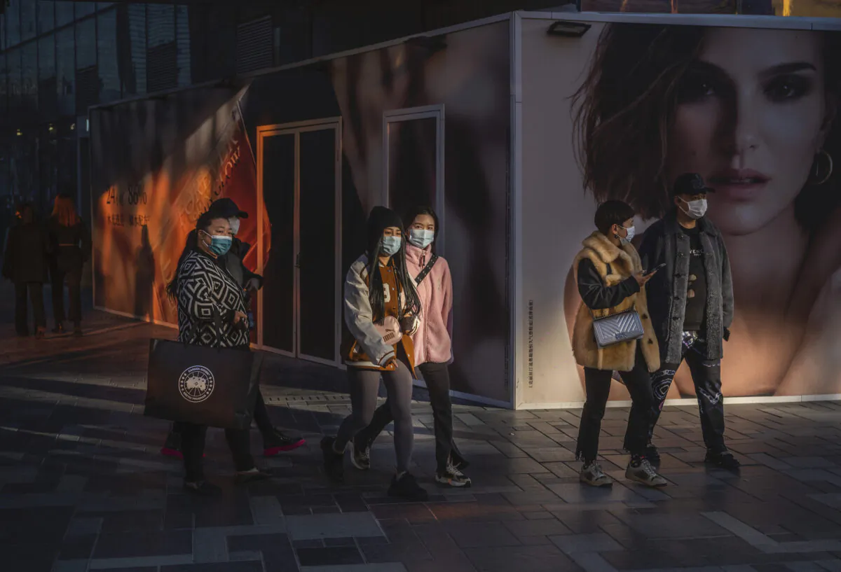 People wear protective masks as they walk by an ad for French luxury fashion brand DIOR outside a new location set to open at a shopping area in Beijing, China, on Nov. 24, 2021. (Kevin Frayer/Getty Images)