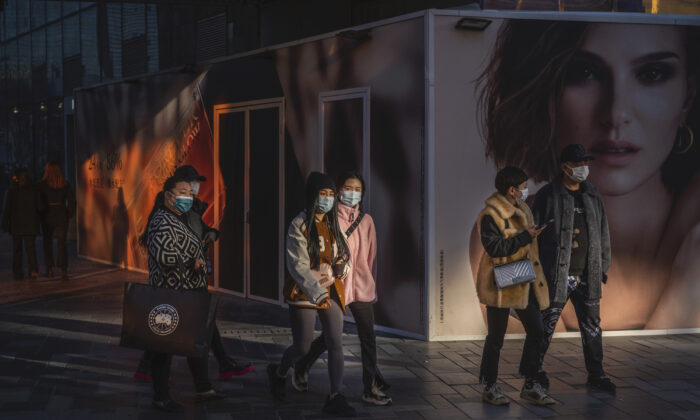 People wear protective masks as they walk by an ad for French luxury fashion brand DIOR outside a new location set to open at a shopping area in Beijing, China, on Nov. 24, 2021. (Kevin Frayer/Getty Images)