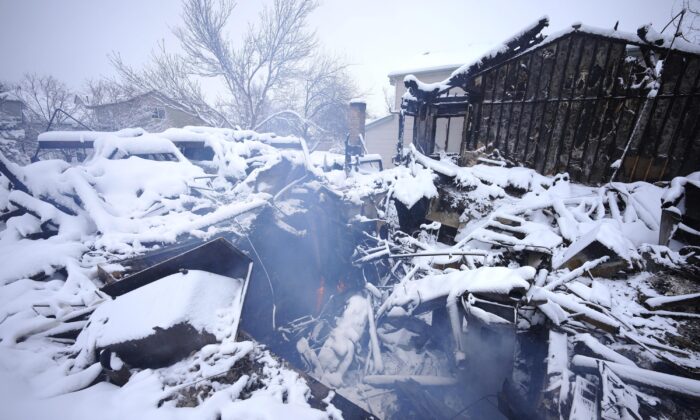 A lone flame flickers as smoke roils from the remains of a home destroyed by a pair of wildfires in Superior, Colo., on Jan. 1, 2022.  (David Zalubowski/AP Photo)