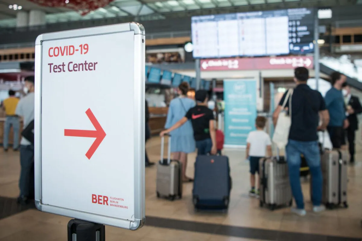Passengers stand with suitcases in front of a display board next to a sign pointing to a test center for COVID-19 at the BER "Willy Brandt" airport in Brandenburg, near Schoenefeld and Berlin in Germany, on July 28, 2021. (Stefanie Loos/AFP via Getty Images)