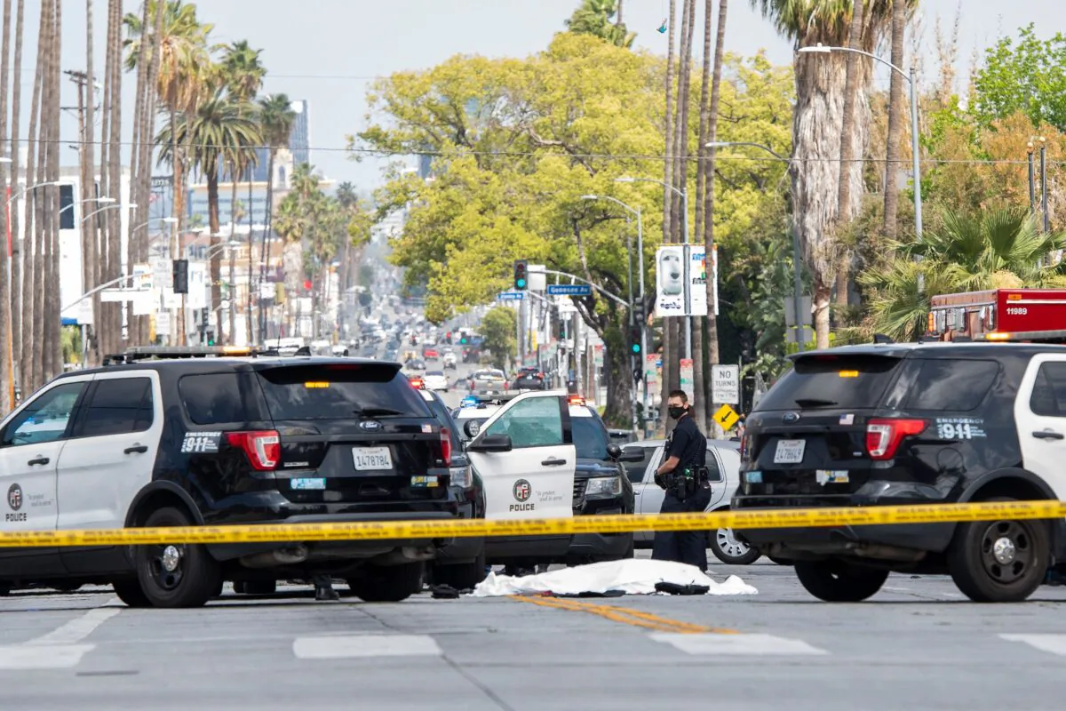 Los Angeles Police Department officers stand at the corner of Fairfax Avenue and Sunset Boulevard where a body covered in a white sheet lies on the pavement in Los Angeles on April 24, 2021. (Valerie Macon/AFP via Getty Images)