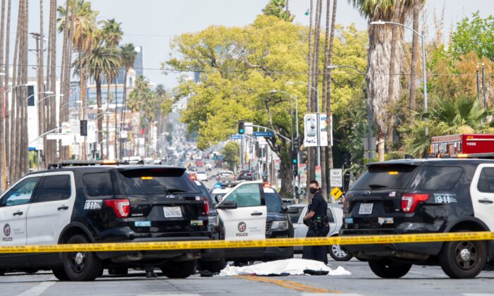 Los Angeles Police Department officers stand at the corner of Fairfax Avenue and Sunset Boulevard where a body covered in a white sheet lies on the pavement in Los Angeles on April 24, 2021. (Valerie Macon/AFP via Getty Images)
