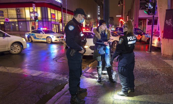Police stop and question a woman at the start of a 10 p.m. to 5 a.m. COVID-19 curfew imposed by the province of Quebec, in Montreal on Dec. 31, 2021. (The Canadian Press/Peter McCabe) 
