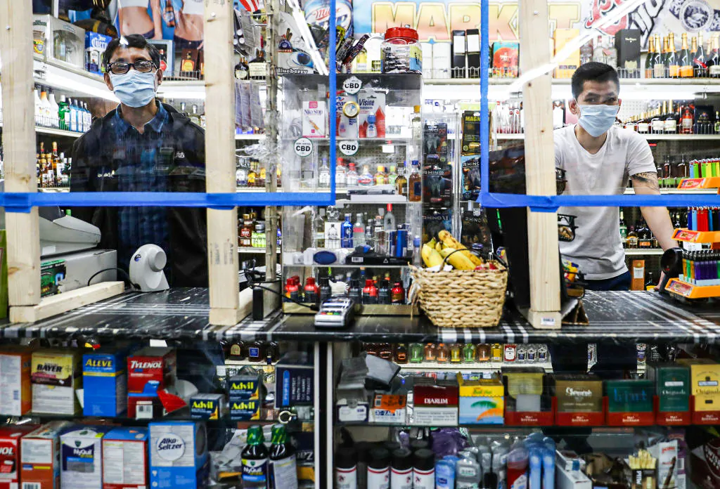 Cashiers wear face masks as they stand behind newly installed plexiglass barriers for protection in a liquor store amid the COVID-19 pandemic in Los Angeles, on April 4, 2020. (Mario Tama/Getty Images)