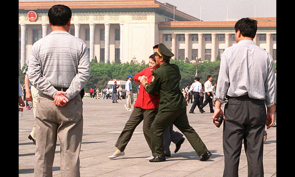 Plainclothes policemen watch as a female practitioner of the Falun Gong spiritual system is being forcefully taken away by Chinese police towards a police van, on May 11, 2000, in Tiananmen Square, Beijing, China. (Stephen Shaver/AFP via Getty Images)﻿
