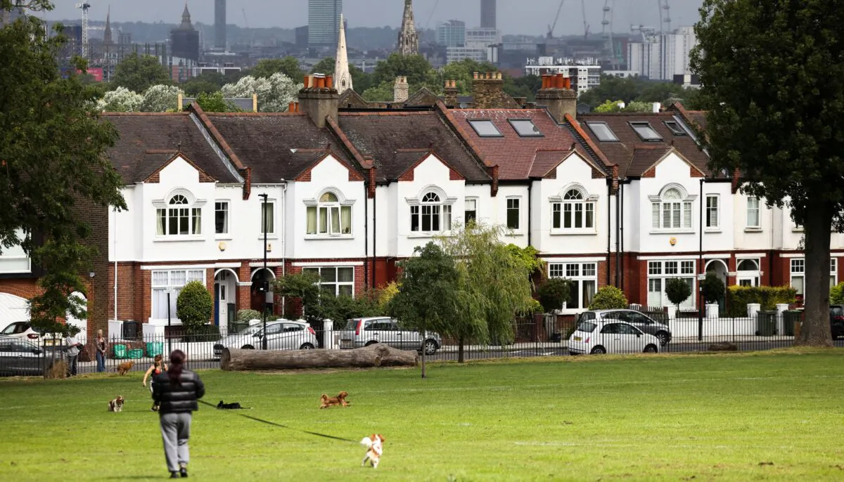 A person walks with a dog in front of a row of residential housing in south London on Aug. 6, 2021. (Henry Nicholls/Reuters)
