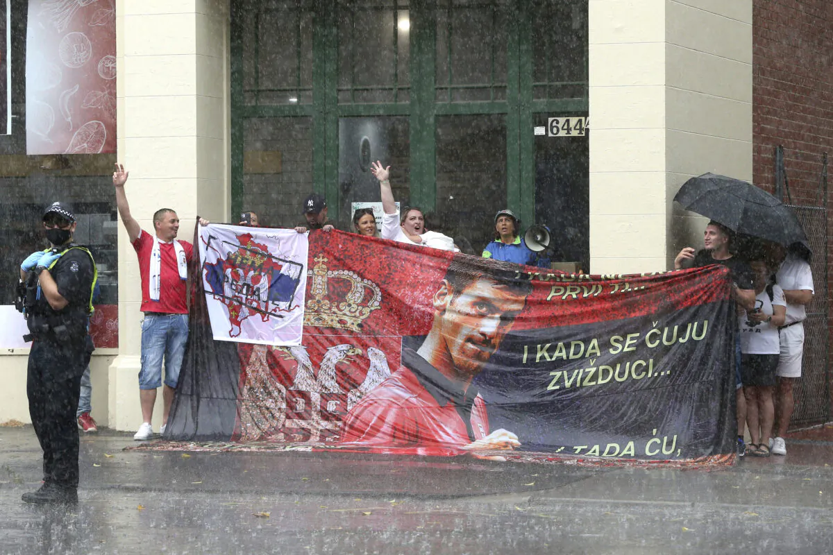 Protestors in the rain outside the Park Hotel in the Melbourne suburb of Carlton ahead of the Australian Open in Melbourne where it is believed Serbia's Novak Djokovic is currently being detained, Australia, on Jan. 7, 2022. (Hamish Blair/AP Photo)