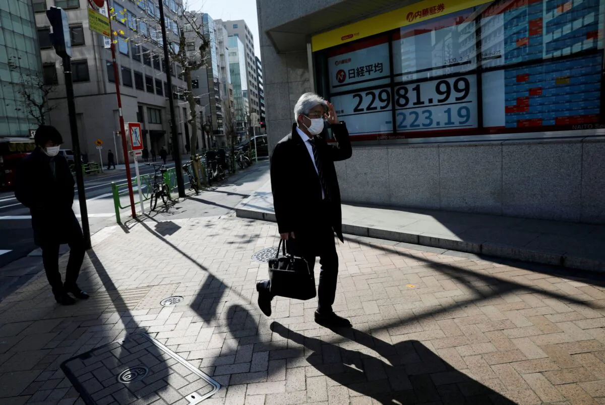 People wearing surgical masks walk past a screen showing Nikkei index outside a brokerage in Tokyo, Japan, on Feb. 3, 2020. (Kim Kyung-Hoon/Reuters)