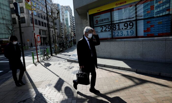 People wearing surgical masks walk past a screen showing Nikkei index outside a brokerage in Tokyo, Japan, on Feb. 3, 2020. (Kim Kyung-Hoon/Reuters)