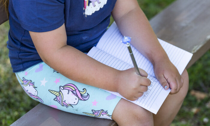 An elementary school student writes in her notebook in Brea, Calif., on May 24, 2021. (John Fredricks/ The Epoch Times)