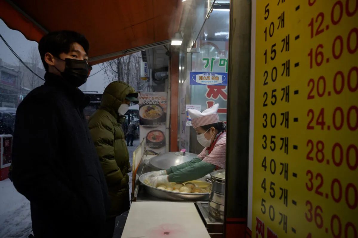 A customer waits as a vendor prepares dumplings at a stall at the entrance to a street market during a snow fall in Seoul on Jan. 12, 2021. (Ed Jones/AFP via Getty Images)