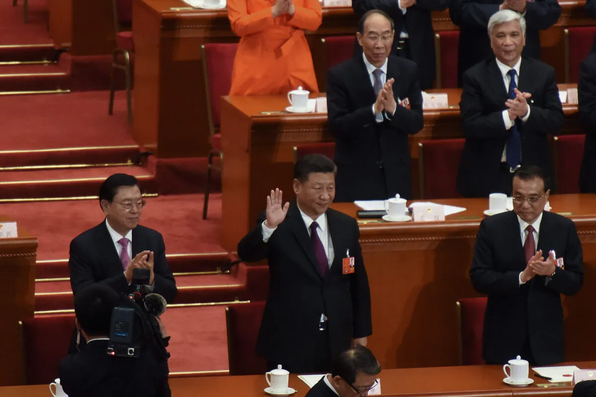 Chinese Communist Party’s head Xi Jinping (C) waves to attendees with Chinese Premier Li Keqiang (R) and member of the Communist Party of China's Politburo Standing Committee Li Zhanshu (L) applauding by his side, after being elected for a second five-year term during the 5th plenary session of the first session of the 13th Congress in Beijing on March 17, 2018. (Etienne Oliveau/Getty Images)