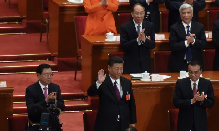 Chinese Communist Party’s head Xi Jinping (C) waves to attendees with Chinese Premier Li Keqiang (R) and member of the Communist Party of China's Politburo Standing Committee Li Zhanshu (L) applauding by his side, after being elected for a second five-year term during the 5th plenary session of the first session of the 13th Congress in Beijing on March 17, 2018. (Etienne Oliveau/Getty Images)