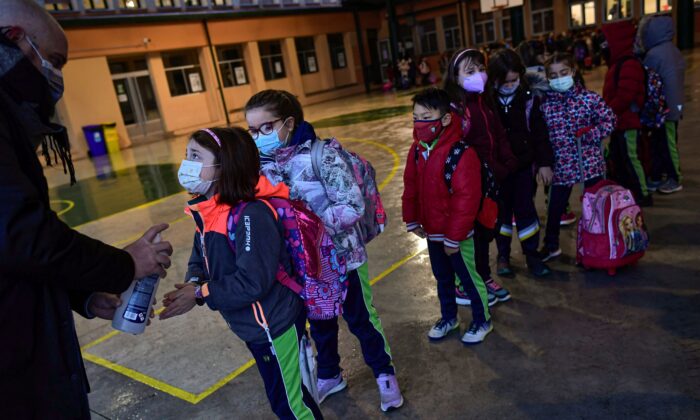 A group of young students wearing face mask protection to prevent the spread of the coronavirus disinfect their hands while waiting in a queue before entering the Luis Amigo school after Christmas holidays, in Pamplona, northern Spain, on Jan. 10, 2022. (Alvaro Barrientos/AP Photo)