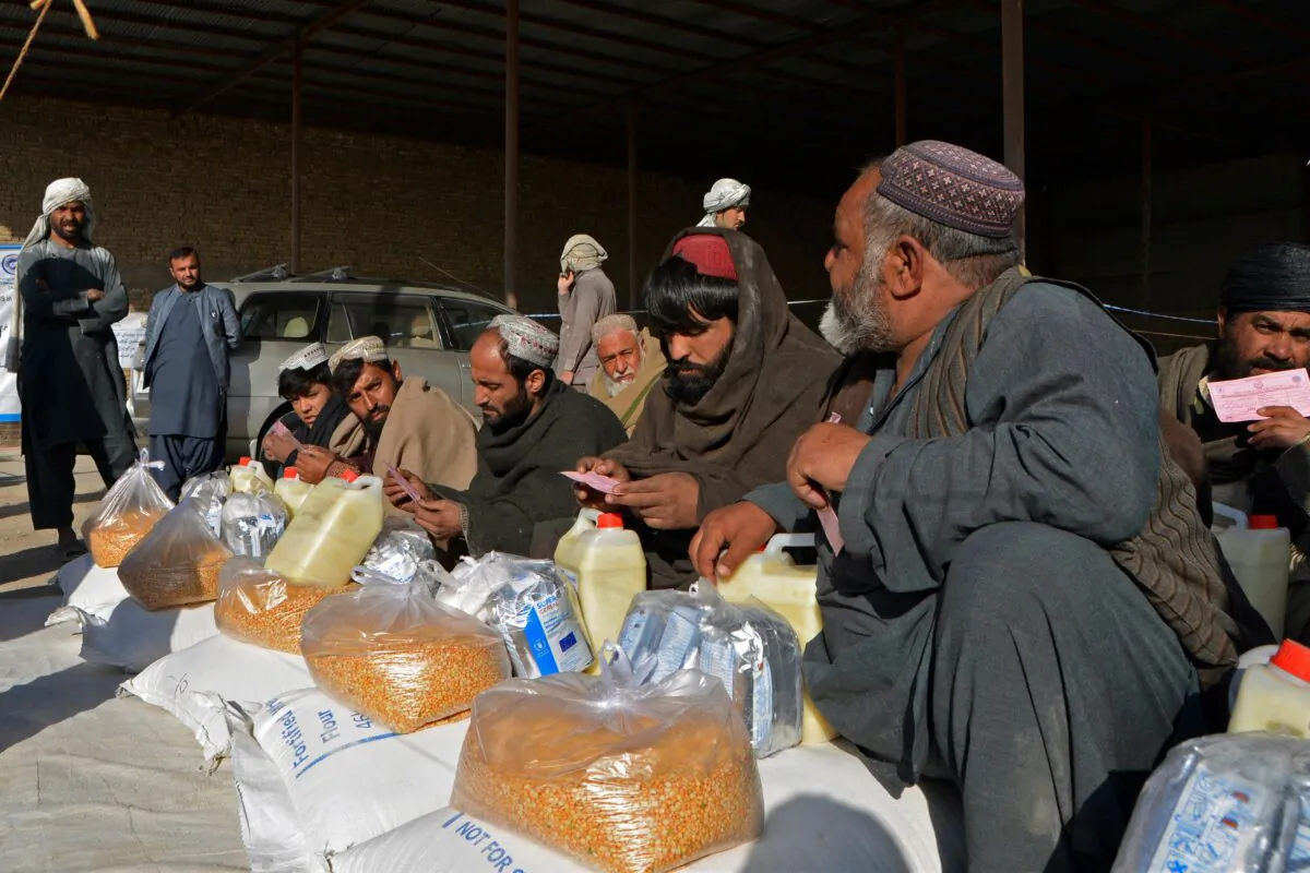 Afghan men sit along with food packets being distributed by the members of World Food Programme (WFP) to the families in need in Kandahar on Dec. 23, 2021. (Javed Tanveer/AFP via Getty Images)