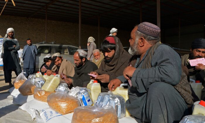 Afghan men sit along with food packets being distributed by the members of World Food Programme (WFP) to the families in need in Kandahar on Dec. 23, 2021. (Javed Tanveer/AFP via Getty Images)